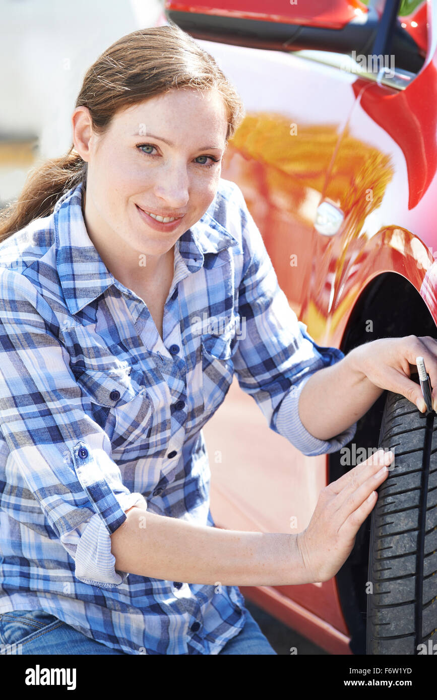 Frau, die Lauffläche auf Pkw-Reifen mit Manometer überprüfen Stockfoto