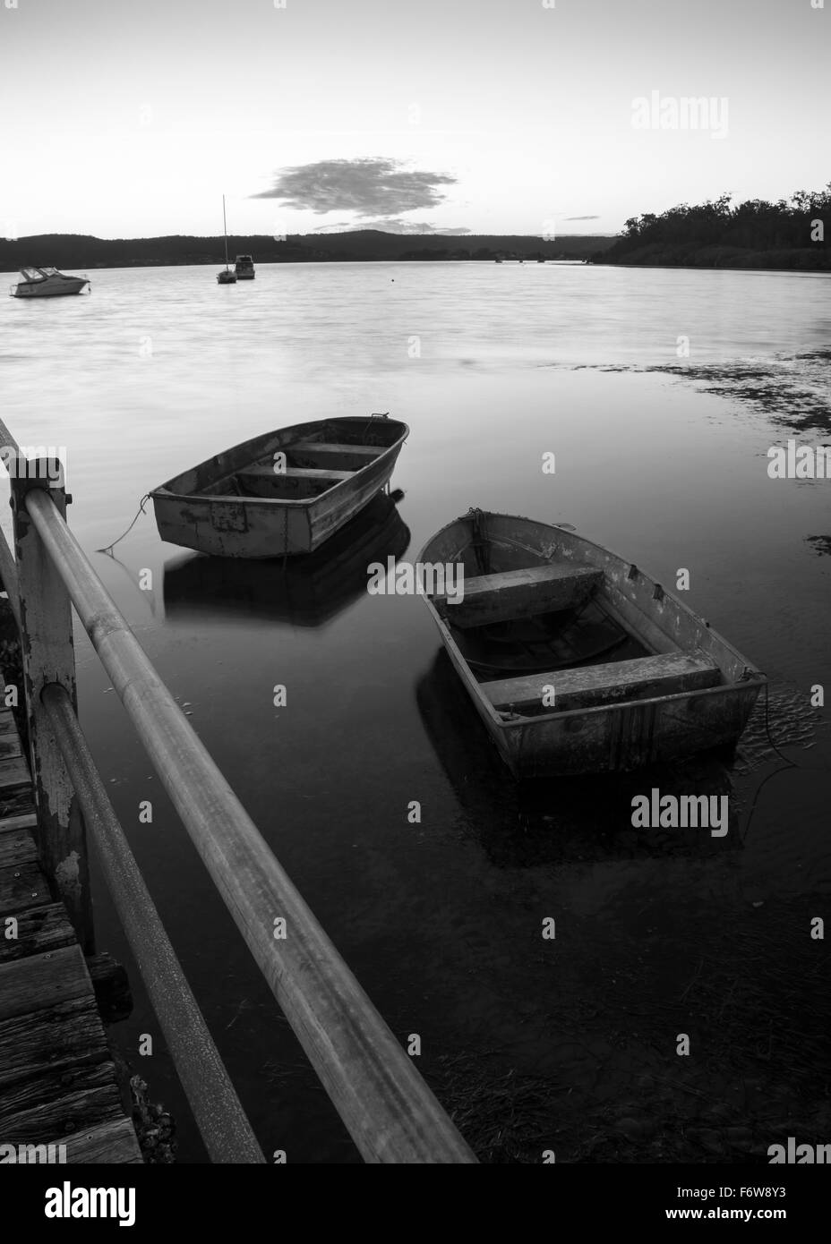 Zwei kleine, offene Schlauchboote (Tinnies) stehen in ruhigem Wasser neben einem Kai der untergehenden Sonne gegenüber. Monochrom Stockfoto