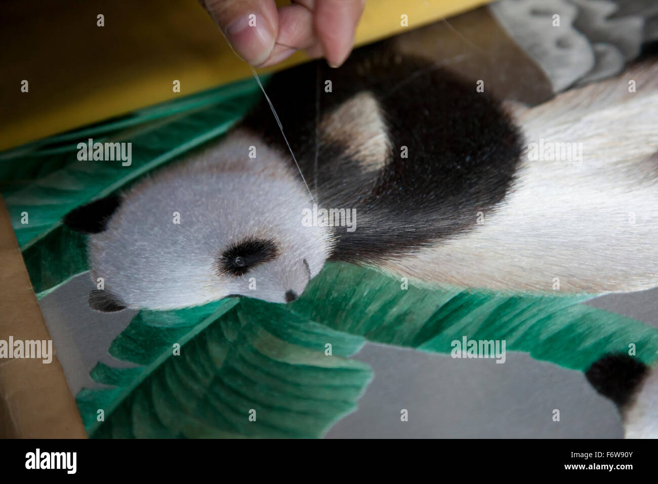 Ein Weber, wodurch eine Stickerei, die eine Panda und grüne Laub im Musée Shu Brokat in Chengdu in Sichuan in China darstellt. Stockfoto