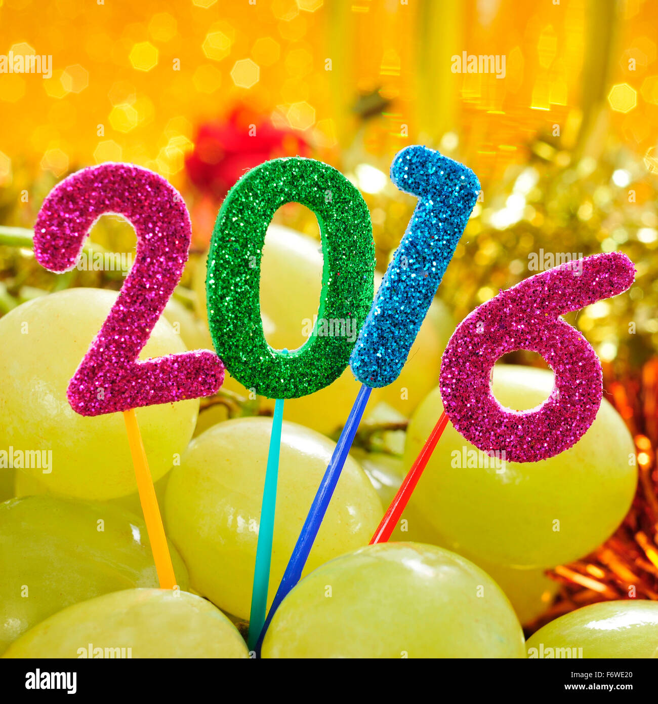 glitzernde Zahlen in verschiedenen Farben bilden die Anzahl 2016, wie das neue Jahr mit einem Haufen von Trauben in einem festlich gedeckten Tisch Stockfoto