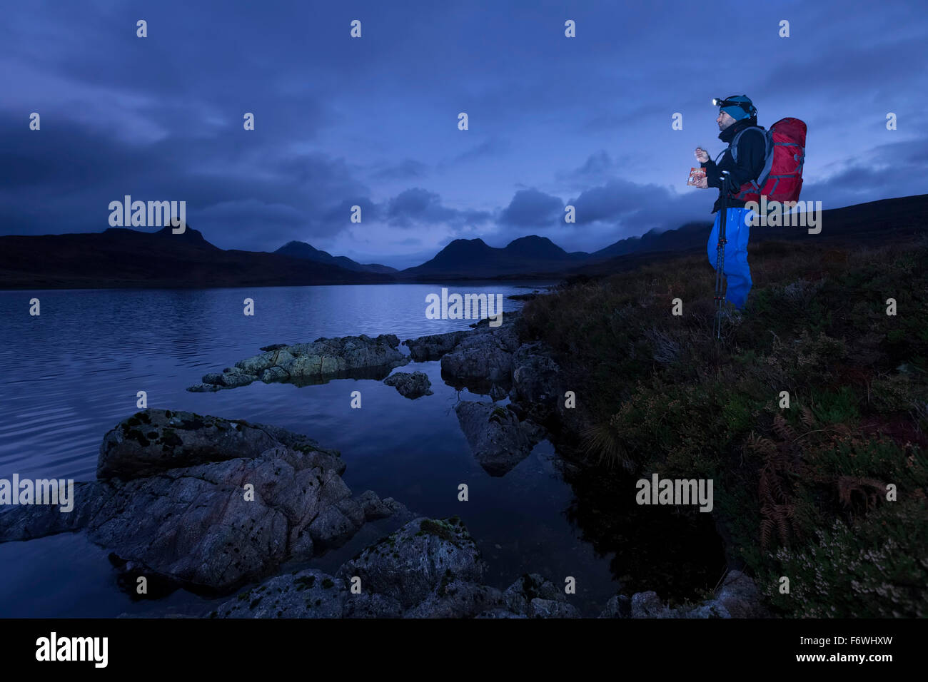 Junger Mann stand am Loch schlecht ein Ghaill in der Abenddämmerung, Stac Pollaidh, Cul Beag, Sgorr Tuath und Ben Mor Coigach im Hintergrund, Assynt, Stockfoto