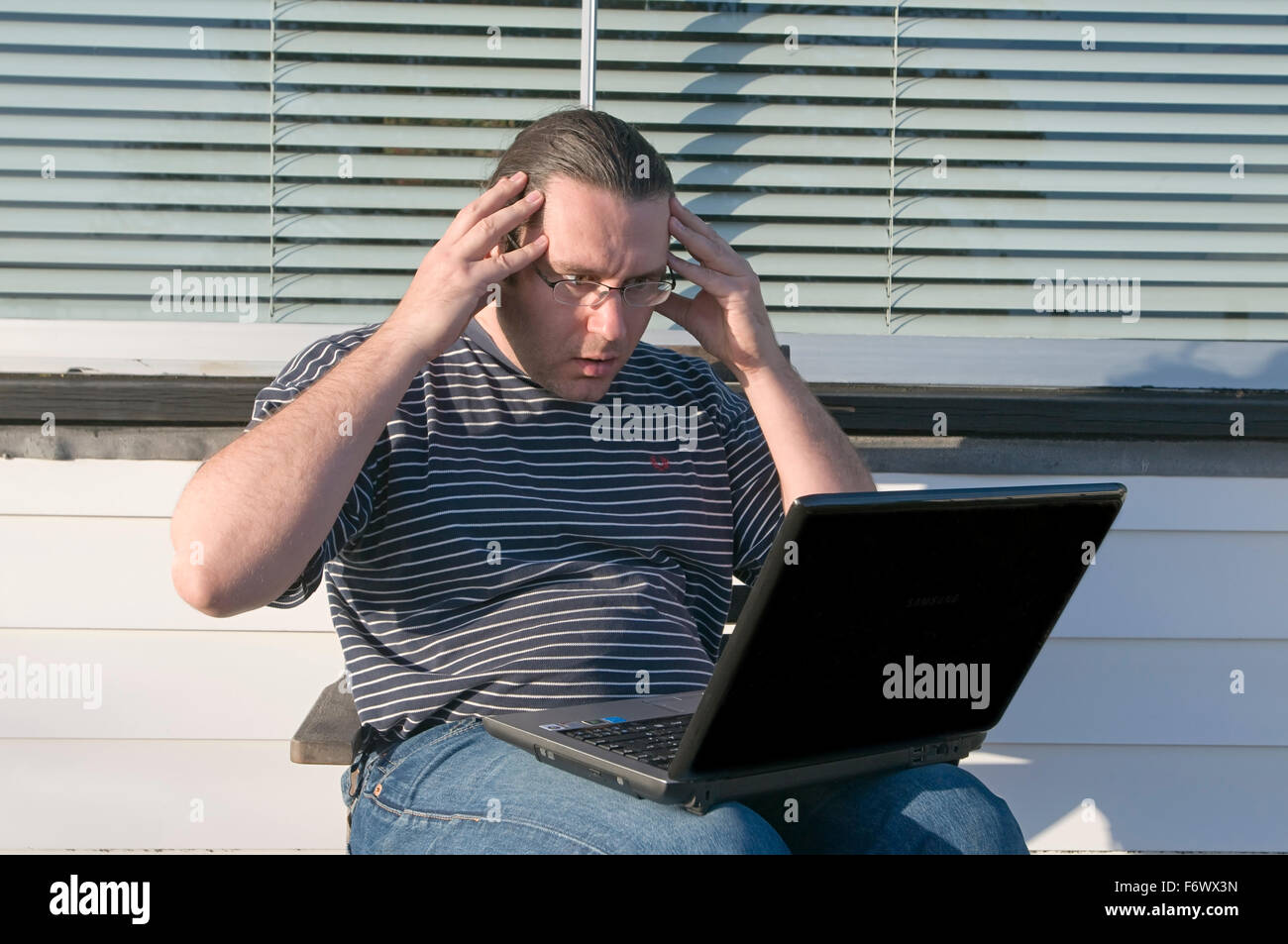 Mann sitzt auf dem Balkon mit einem laptop Stockfoto