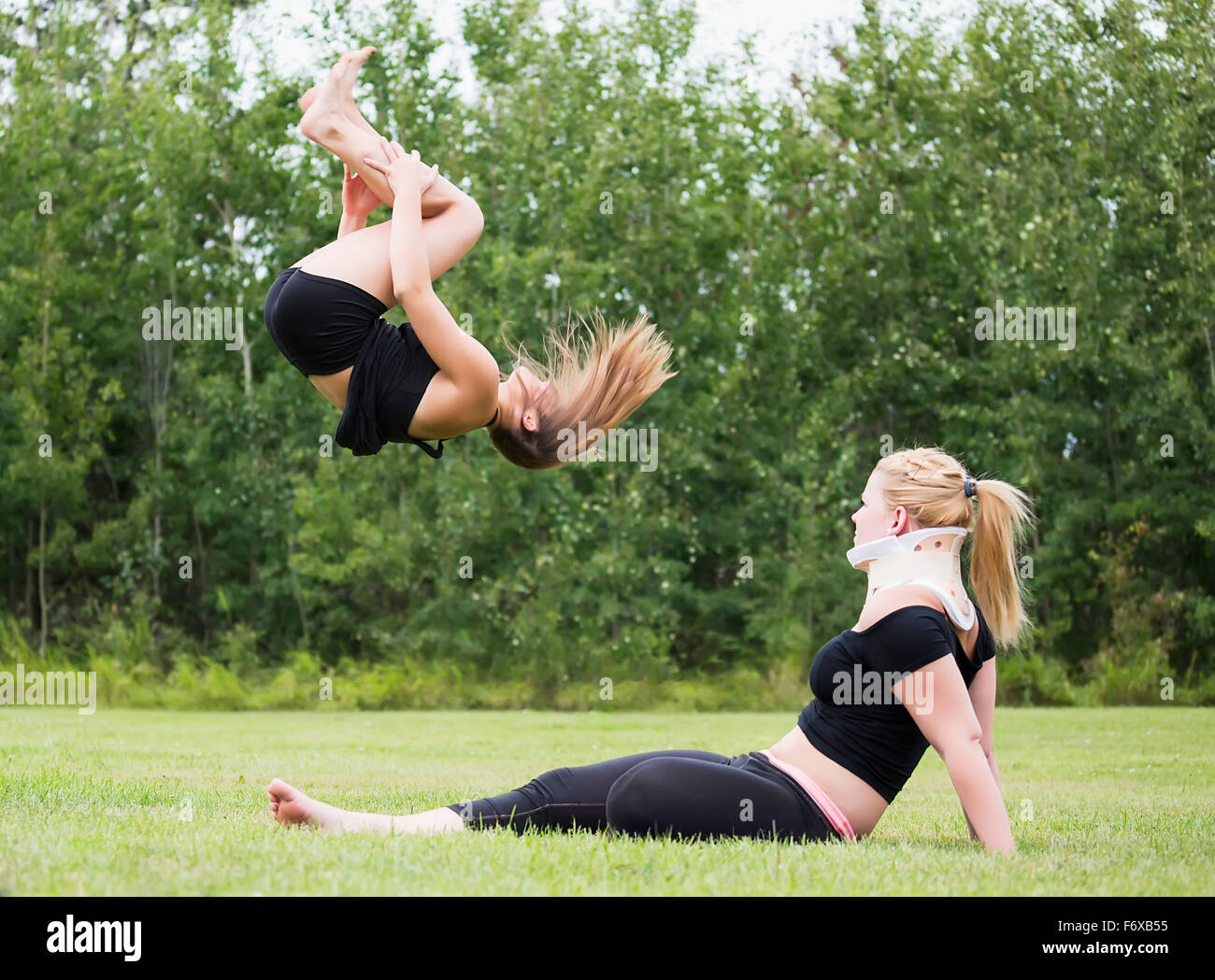 Ein Teenager Turnerin üben ihren Rücken stecken im Freien in einem Park während ihres verletzten Partner Uhren; Edmonton, Alberta, Kanada Stockfoto