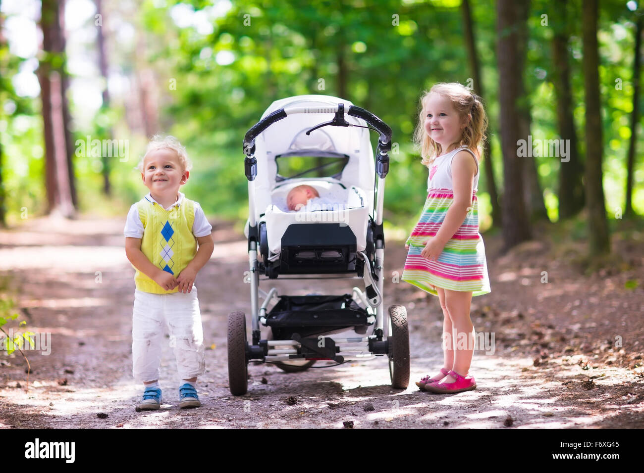 Jungen und Mädchen gehen in sonnigen Sommerpark schieben Kinderwagen mit