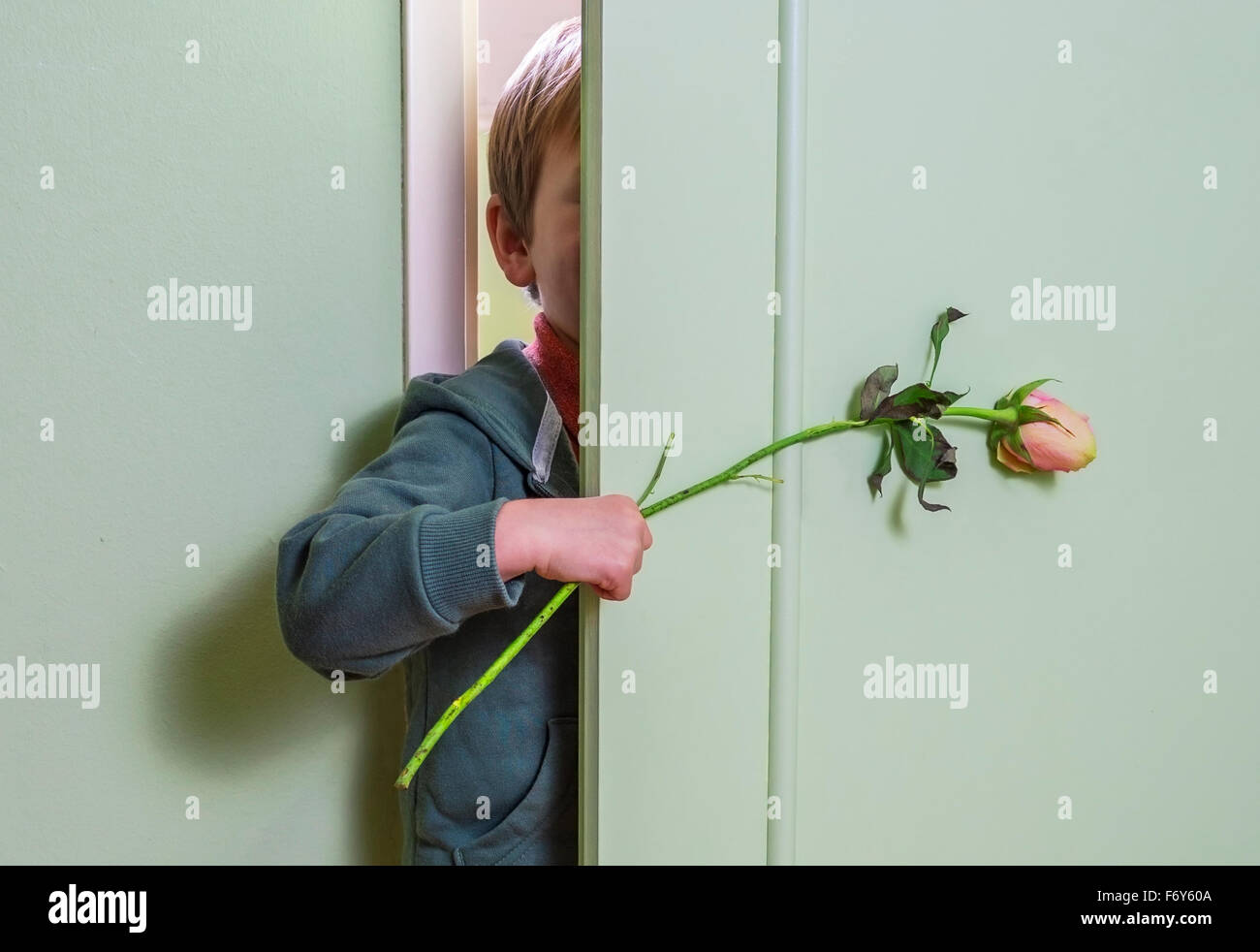 kleines Kind versteckt sich hinter der Tür und hält eine Blume Stockfoto