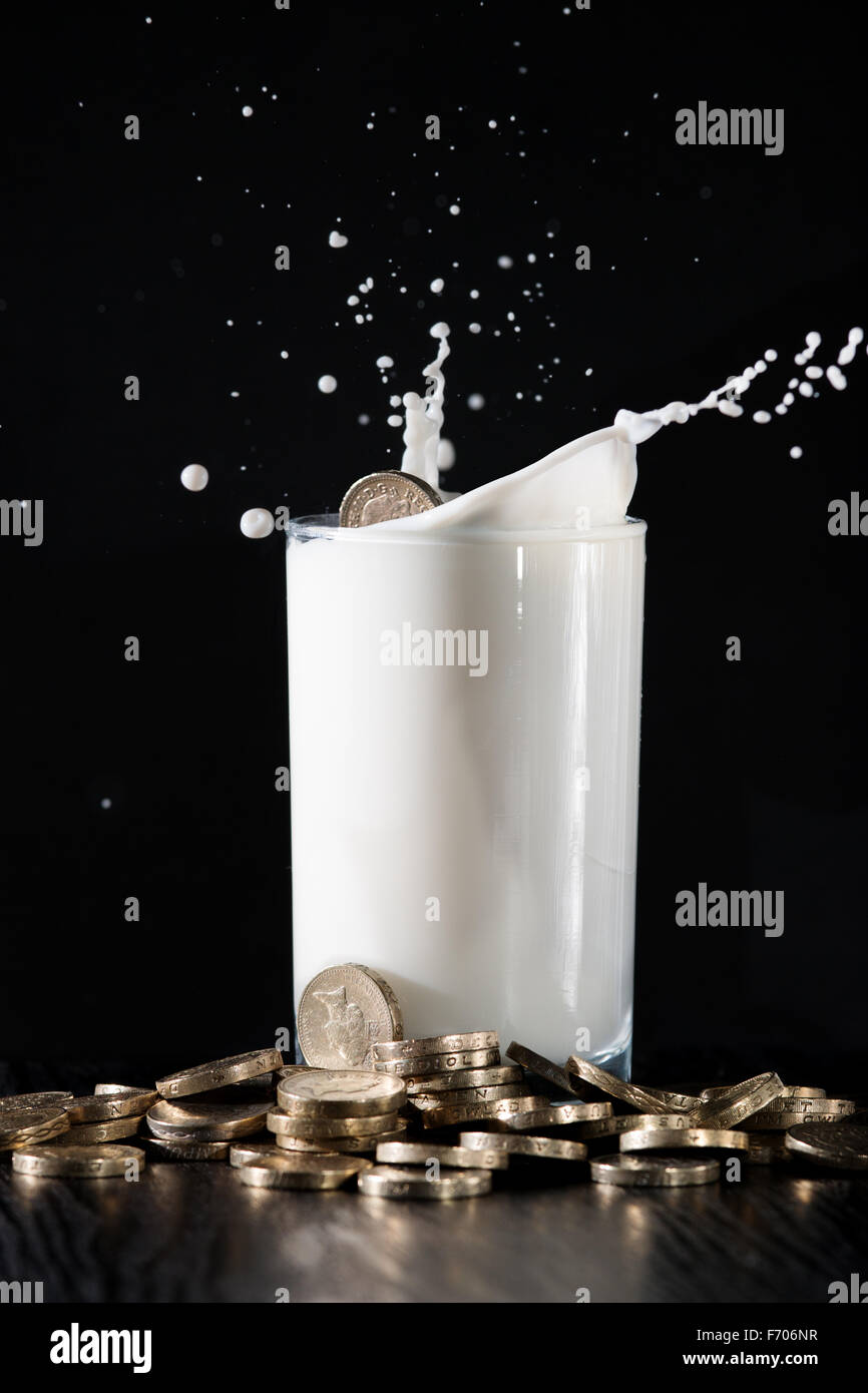Eine Pfund-Münze fiel in ein Glas Milch auf einem Tisch mit Geld angehäuft. Stockfoto