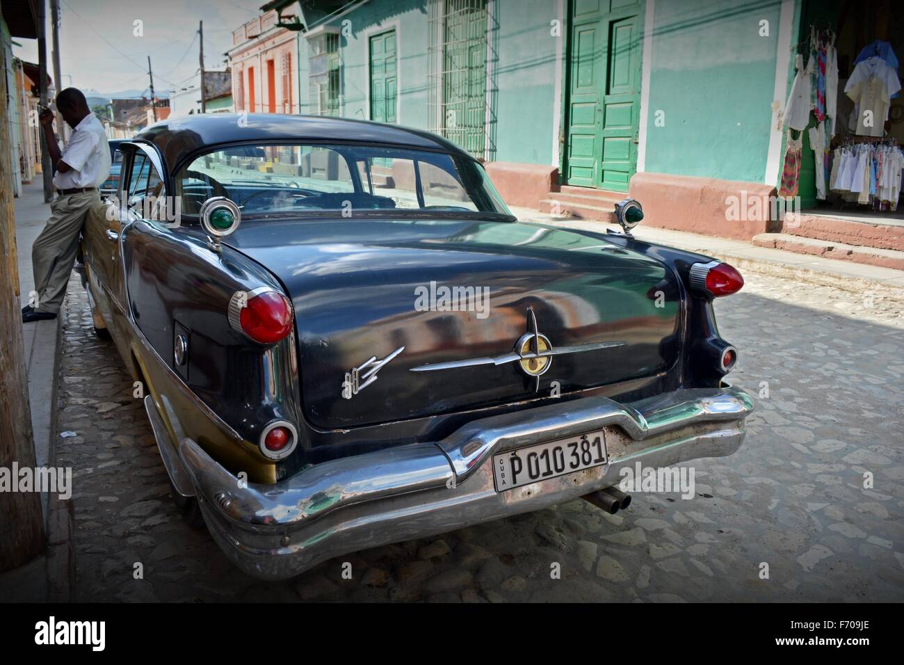 Fahrer, stützte sich auf geparkte Oldtimer mit einer Zigarette brechen im Schatten an einem sonnigen gepflasterten Straße in Trinidad Südwesten Kuba Stockfoto