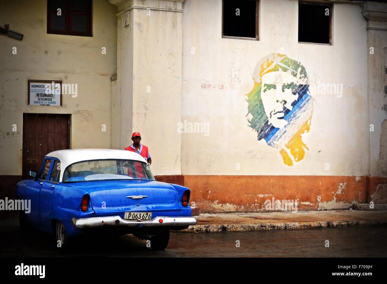 blaue und weiße Oldtimer mit Parkservice geparkt neben dem Che Guevara Wandbild an einem regnerischen Tag in Havanna Kuba Stockfoto