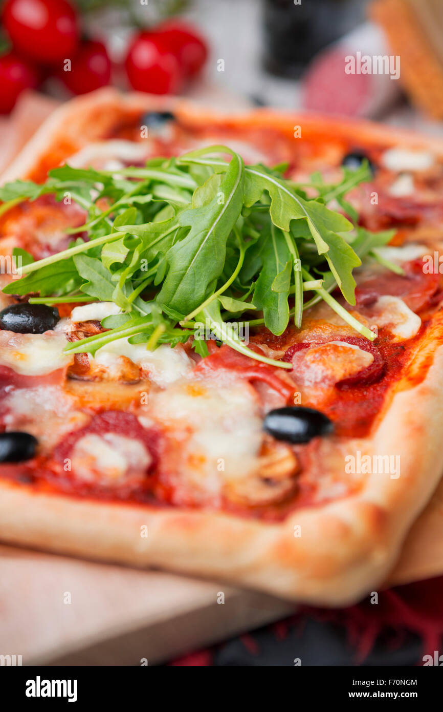 Hausgemachte rechteckige Peperoni-Pizza auf einem rustikalen Tisch mit Zutaten. Stockfoto