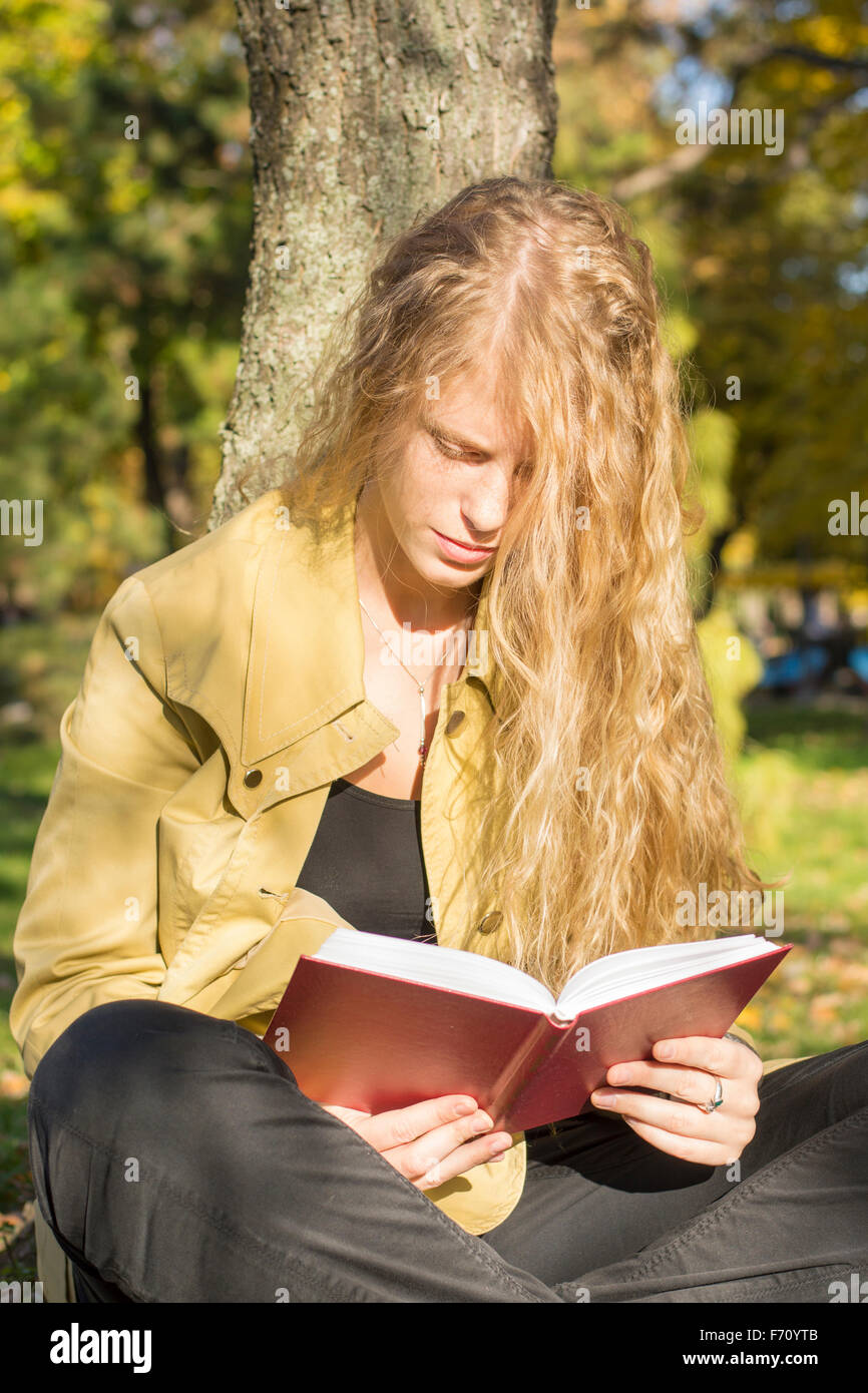 Blondes Mädchen in einem roten Buch in einem Park an einem sonnigen Tag Stockfoto