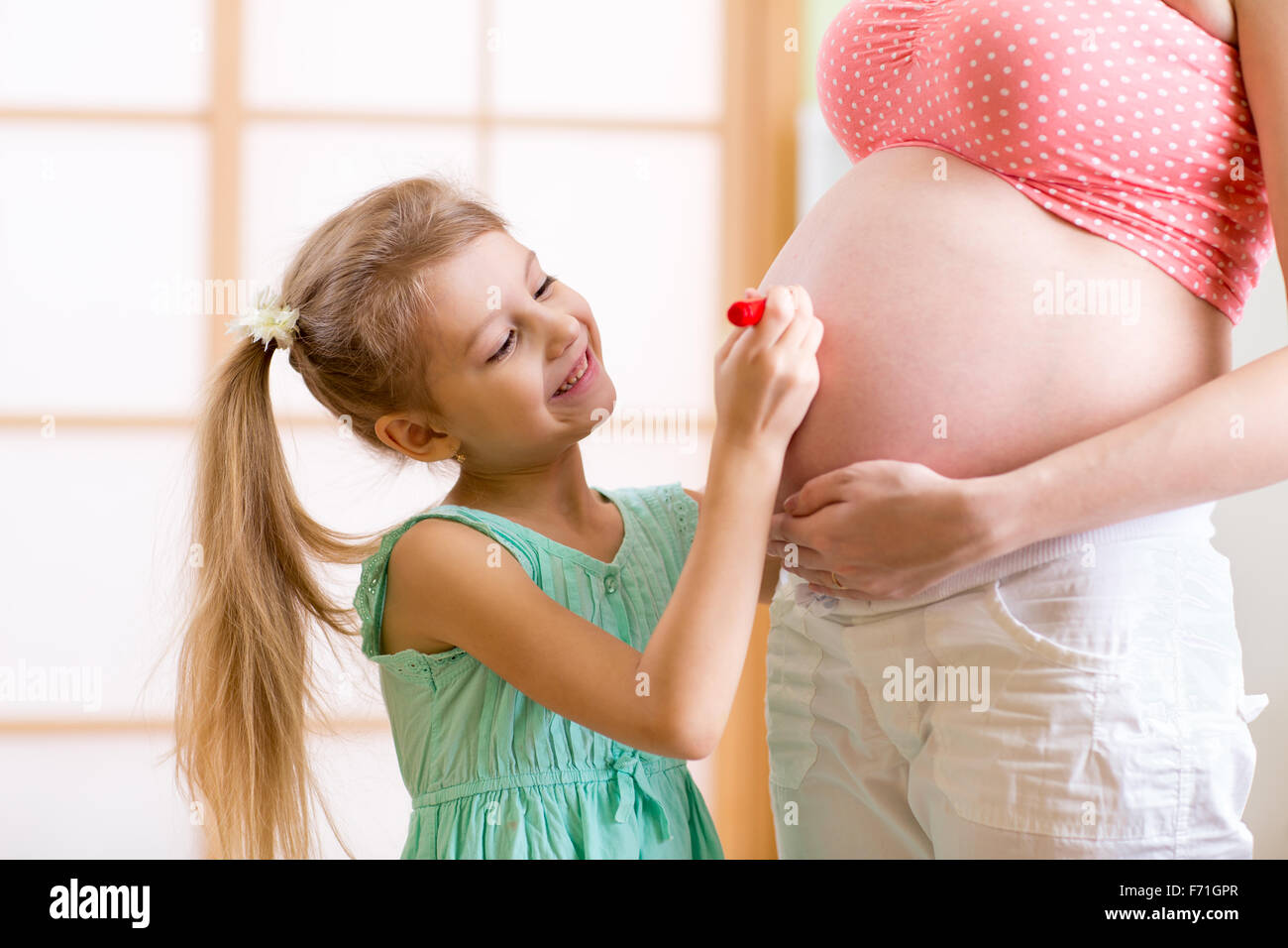 Kind-Tochter Malerei auf Bauch der schwangeren Mutter Stockfoto