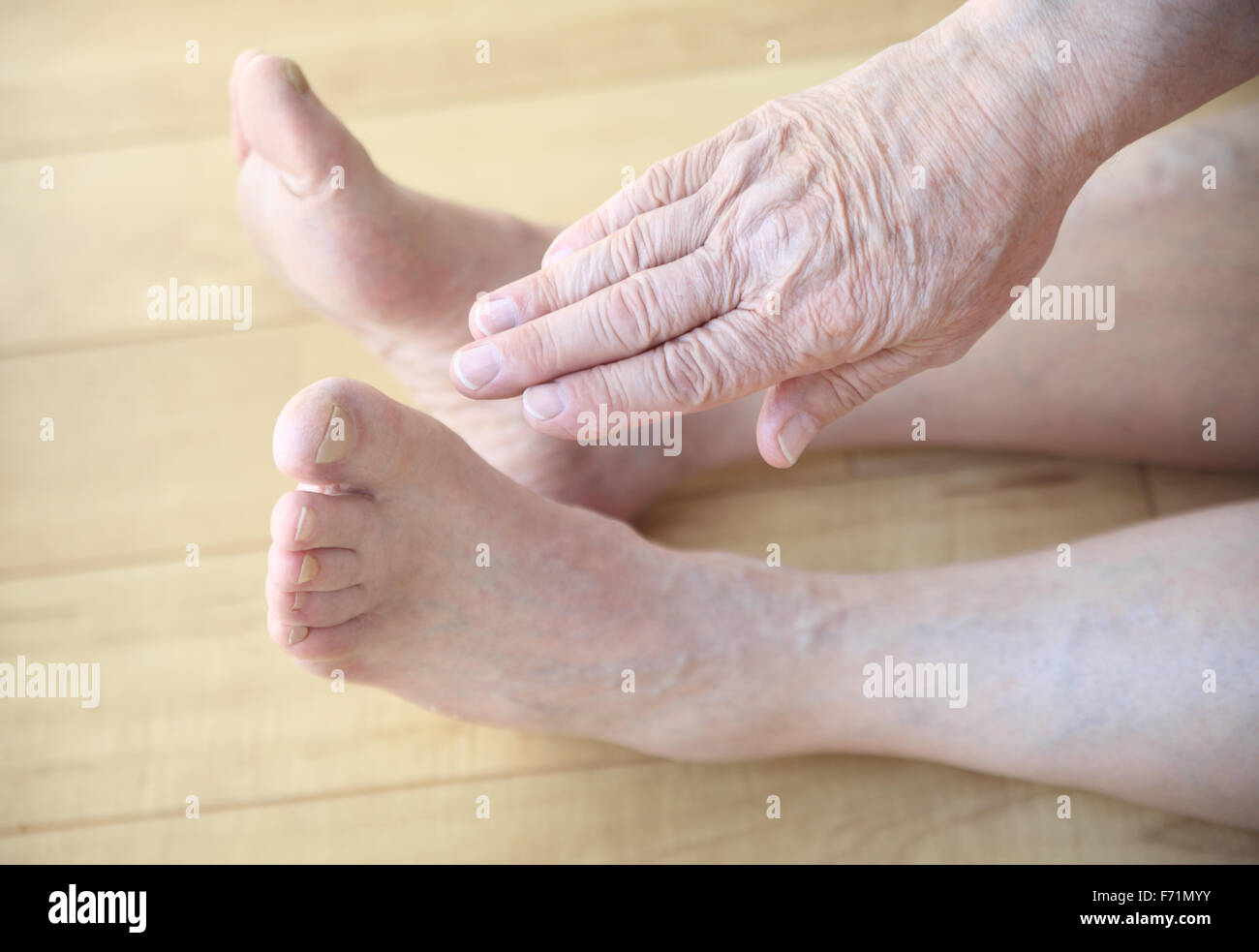 Eine sitzende senior woman erstreckt sich eine Hand in Richtung seiner Zehen. Stockfoto