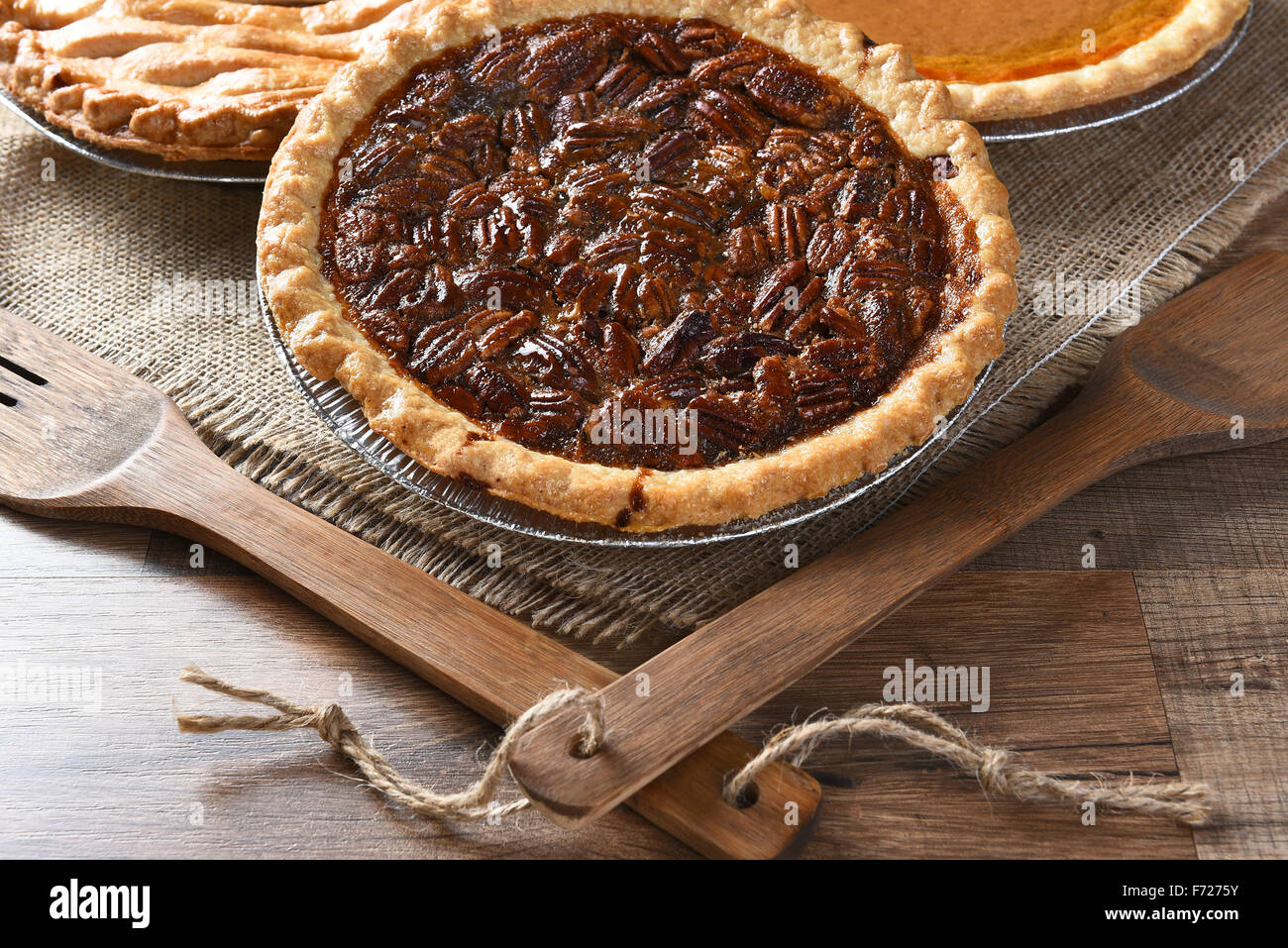Nahaufnahme eines frisch gebackenen Pecan Pie mit Holz Geschirr und Sackleinen Tischdecke. Zwei weitere Torten im Hintergrund Thanksgiving Stockfoto