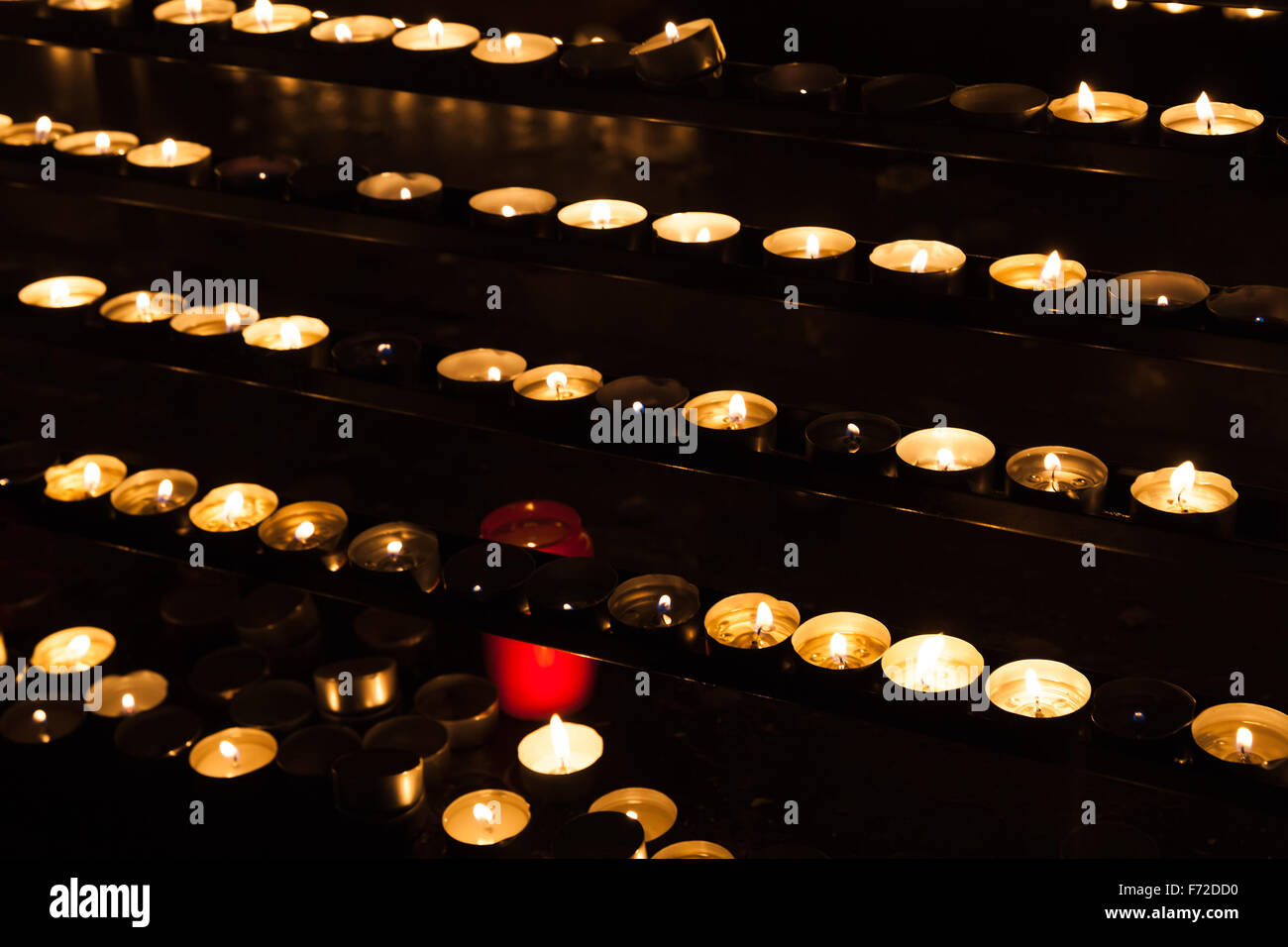 Kleine Kerzen in Reihen brennen in den Regalen in dunklen katholische Kirche Stockfoto
