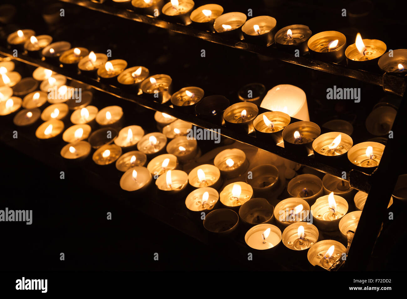 Große Gruppe von kleinen Kerzen brennen in den Regalen in dunklen katholische Kirche Stockfoto