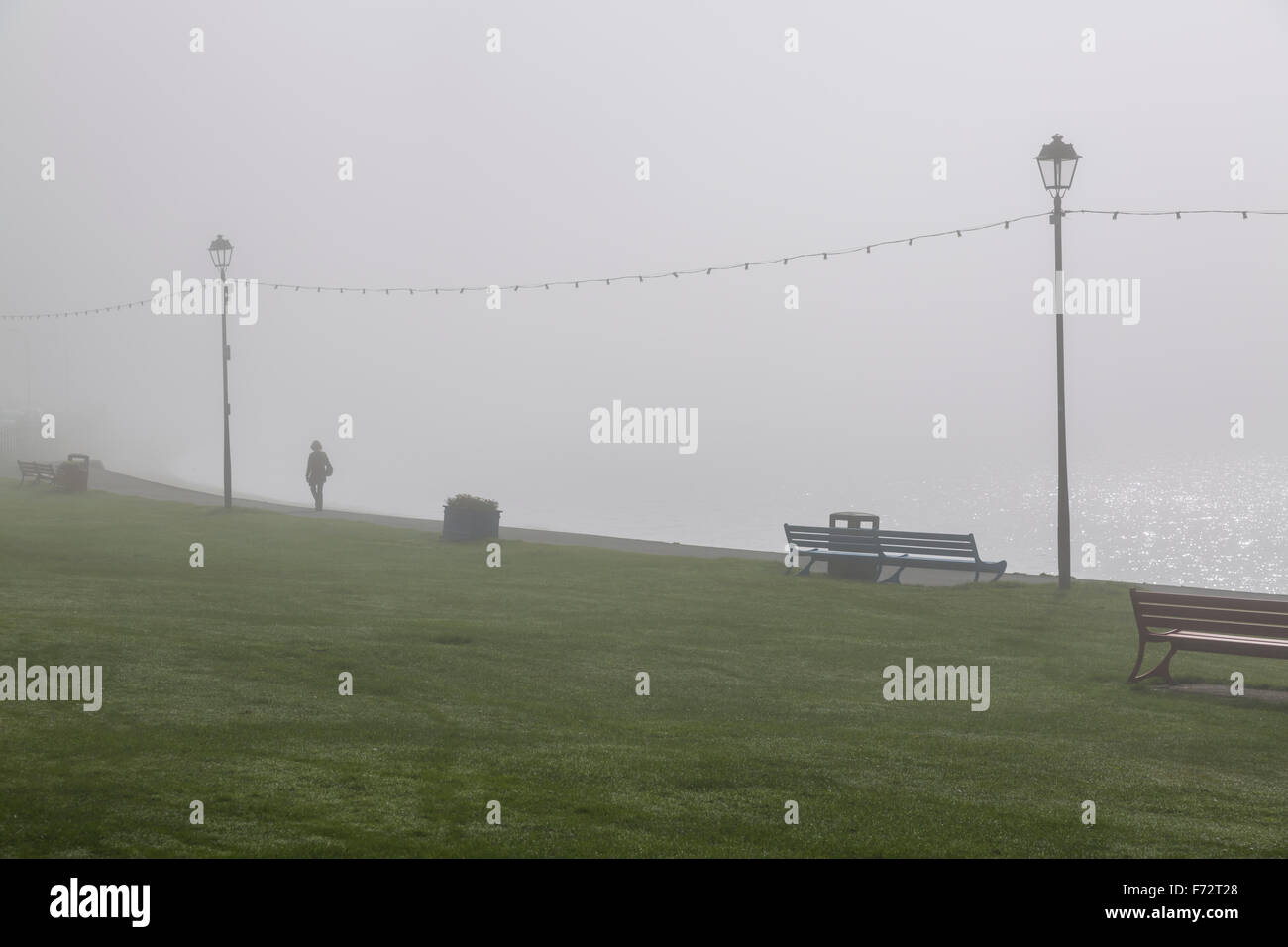 Eine Person, die zwischen Laternenpfosten an einer Strandpromenade im Nebel, Largs, North Ayrshire, Schottland, Großbritannien, läuft Stockfoto