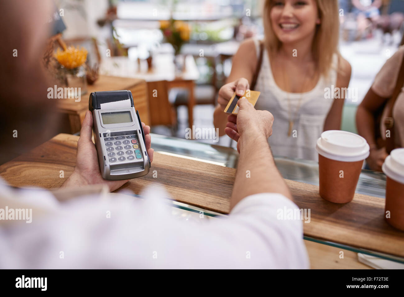 Kunden bezahlen ihre Bestellung mit einer Kreditkarte in einem Café. Barkeeper Besitz einer Kreditkarte Leser-Maschine und die Rückkehr der d Stockfoto