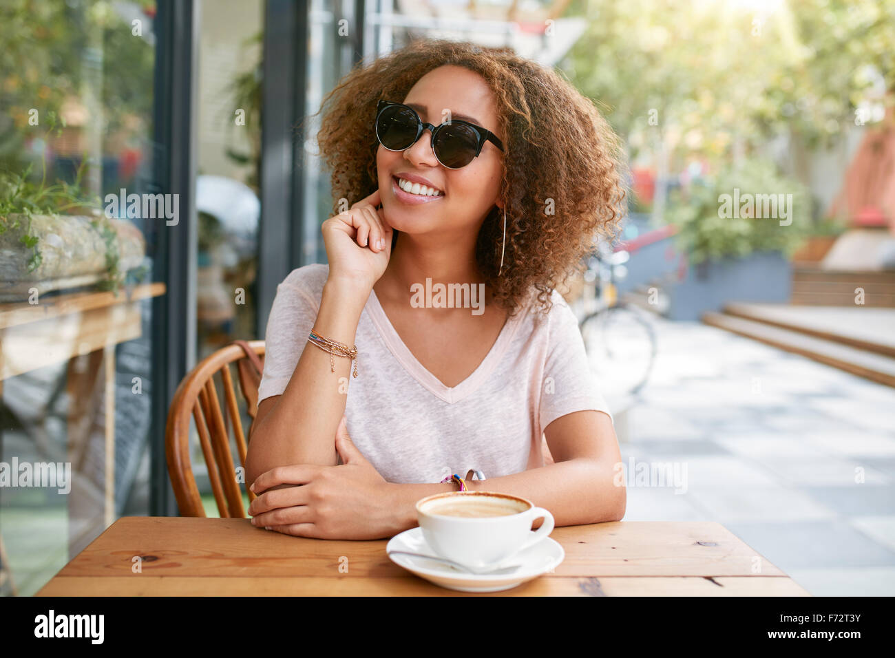 Porträt von netten jungen Mädchen sitzen im Café im freien Blick in die Kamera und lächelnd. Junge Afrikanerin im Straßencafé mit einem c Stockfoto