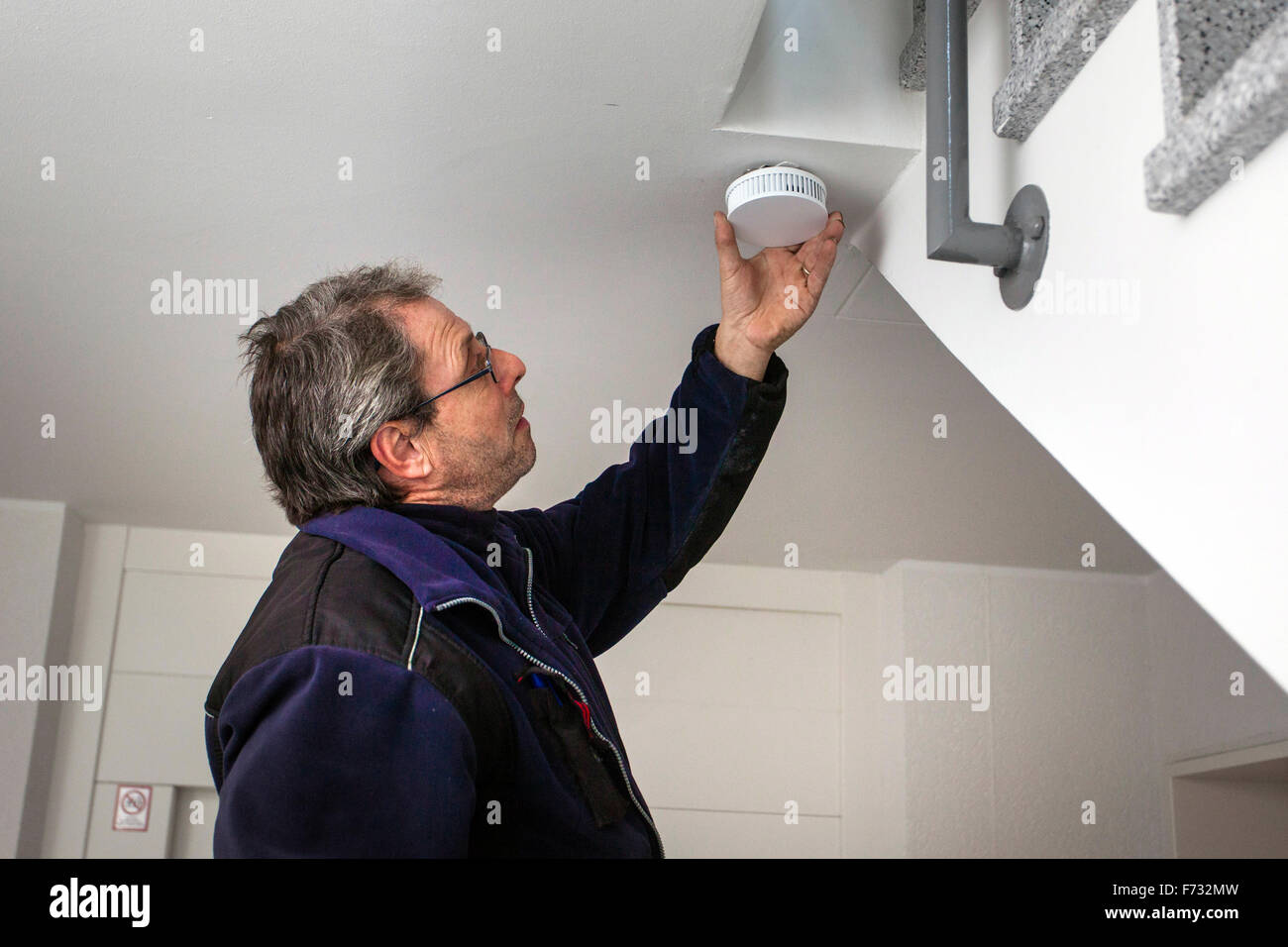 Hausmeister in einem Treppenhaus montiert und überprüft einen Rauchmelder  Stockfotografie - Alamy