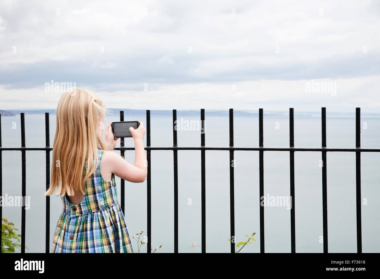 Ein Mädchen in einem aufgegebenen Sommerkleid mit dem Fotografieren mit einem Smartphone. Stockfoto