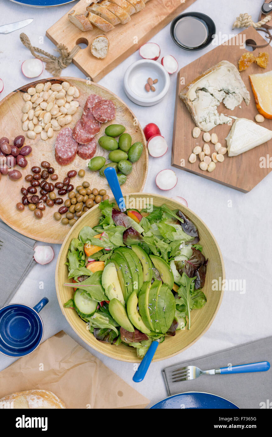Vogelperspektive Blick auf eine Käseplatte, Käse, Oliven, Nüssen und eine Schüssel mit Salat auf dem Tisch. Stockfoto