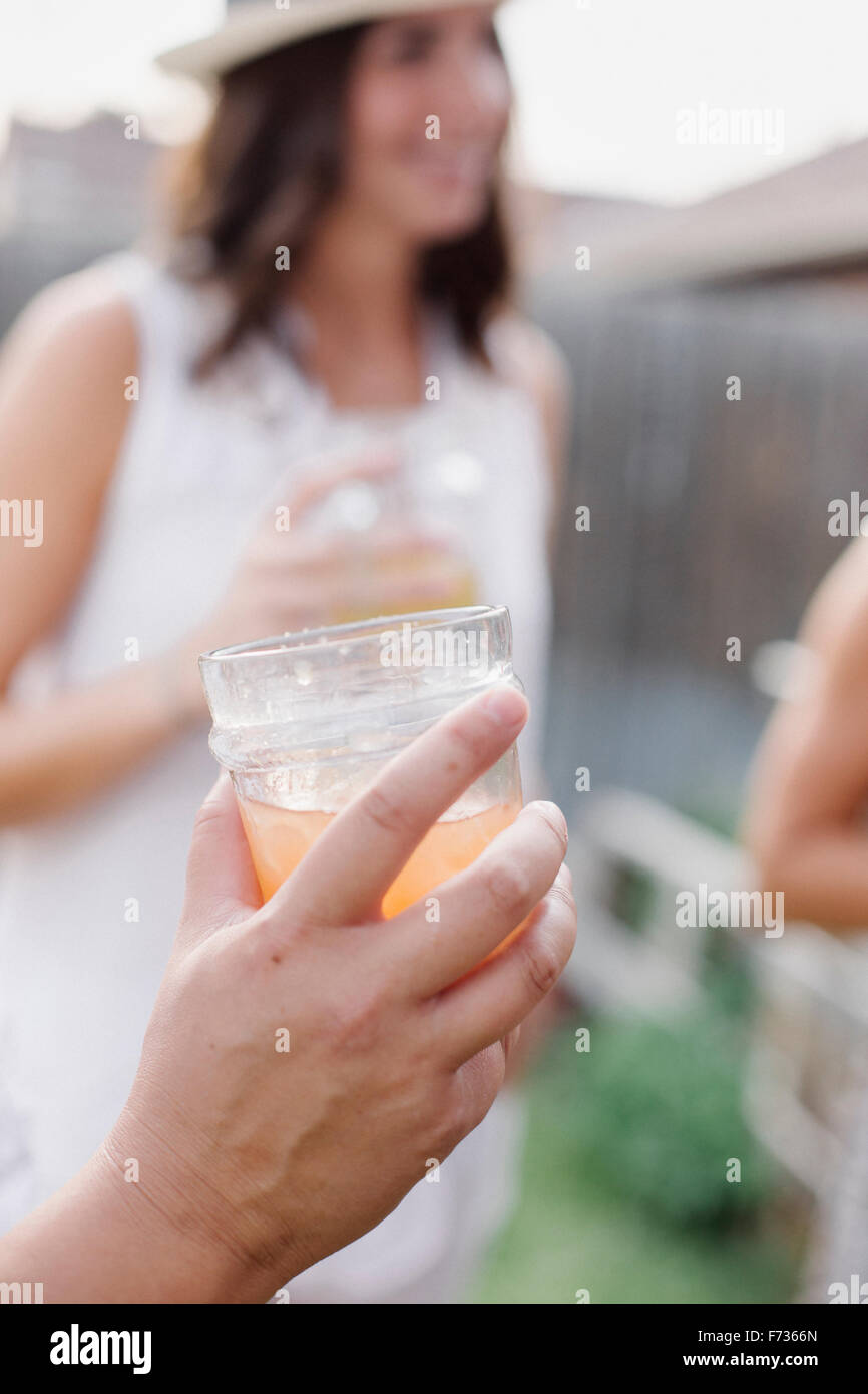 Nahaufnahme von einer Hand hält einen Drink, eine Frau im Hintergrund. Stockfoto