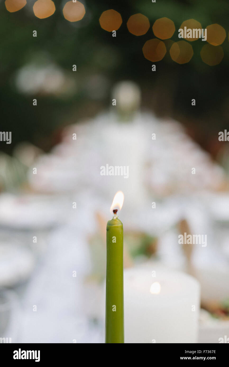 Eine brennende Kerze auf einem Tisch set mit Teller und Gläser, Essen und trinken in einem Garten. Stockfoto