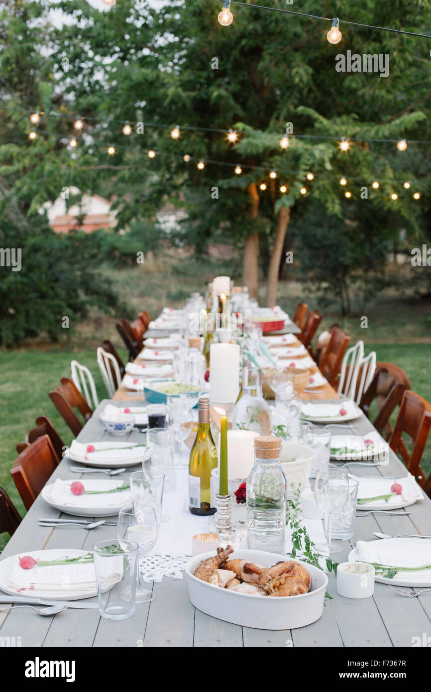 Langer Tisch set mit Teller und Gläser, Essen und trinken in einem Garten. Stockfoto