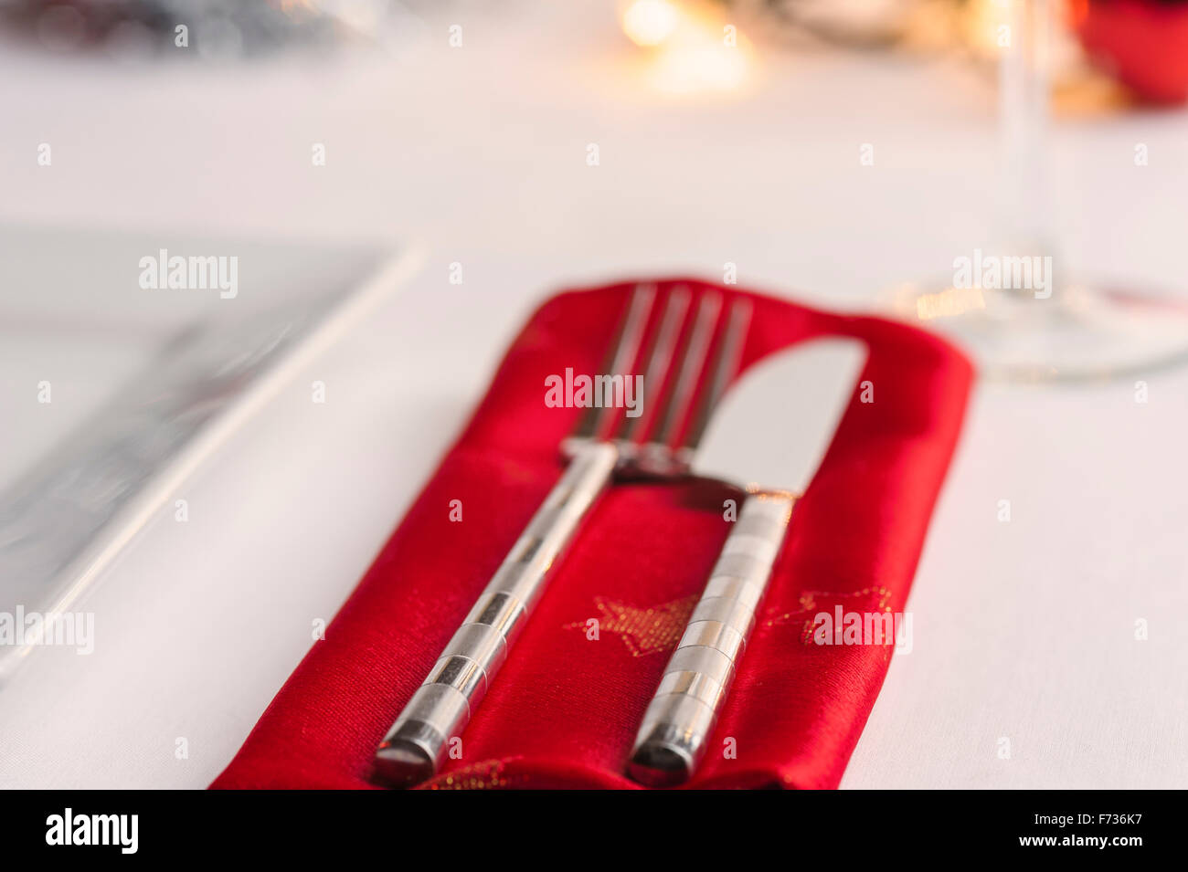 Tabelle festgelegt für das Weihnachtsessen, mit Kugeln und Lametta und Lichterketten dekoriert. Messer, Gabel und rot Serviette. Stockfoto