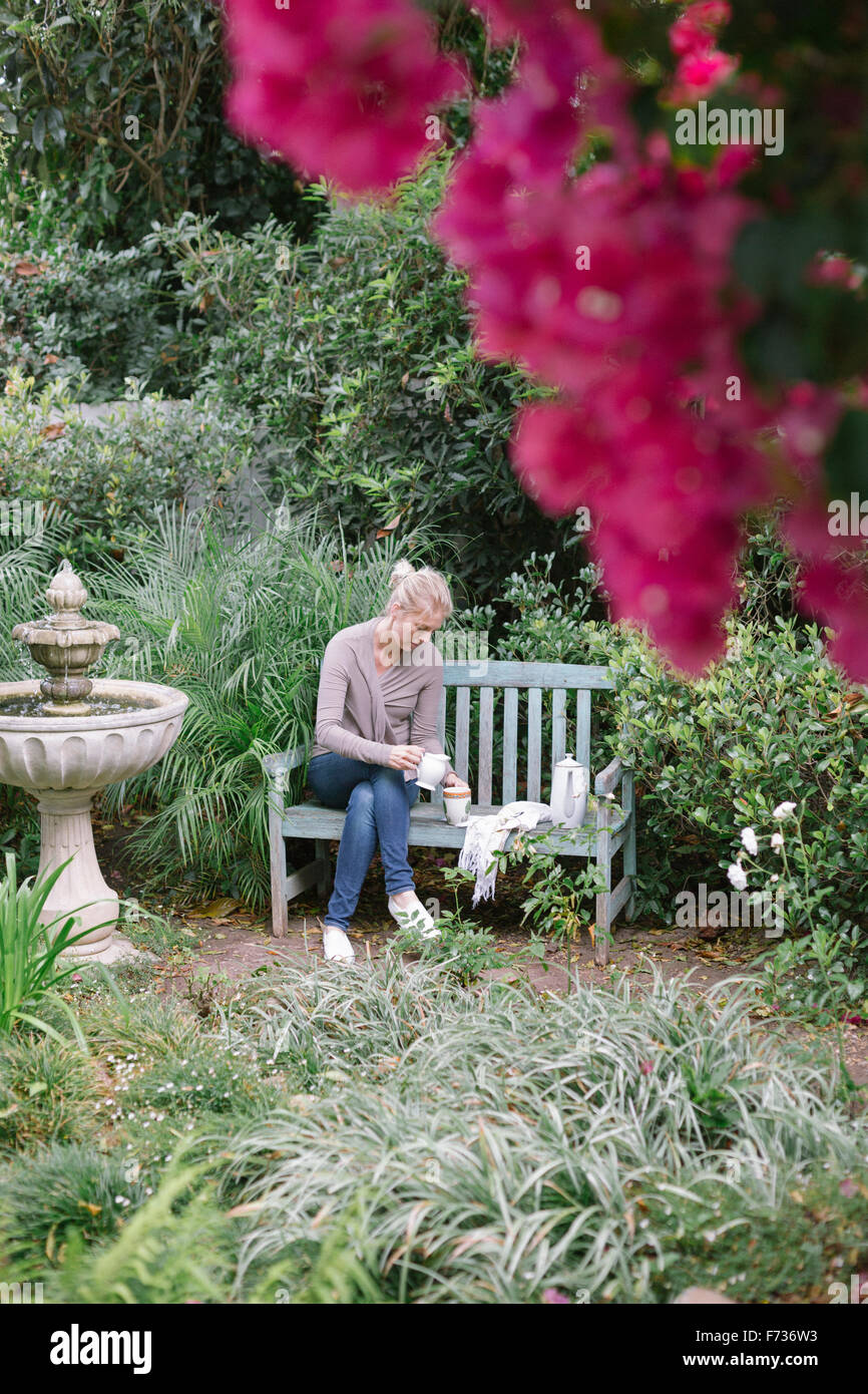 Frau sitzt auf einer Holzbank in einem Garten eine Pause. Stockfoto