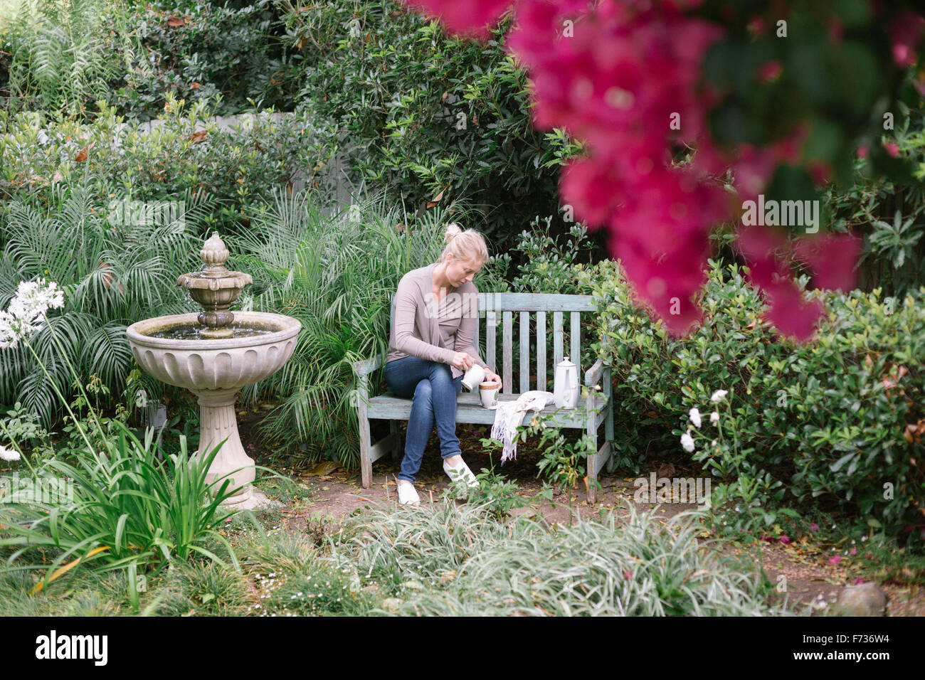 Frau sitzt auf einer Holzbank in einem Garten eine Pause. Stockfoto