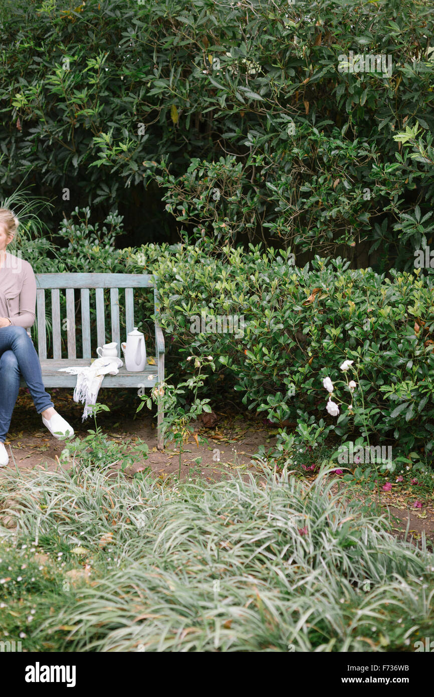 Frau sitzt auf einer Holzbank in einem Garten eine Pause. Stockfoto