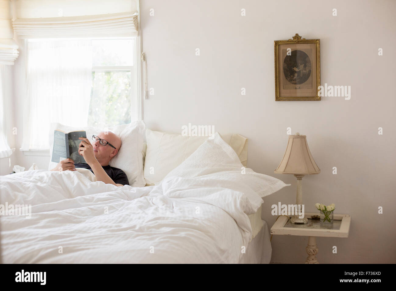 Mann liegt im Bett mit weißem Leinen, lesen. Stockfoto