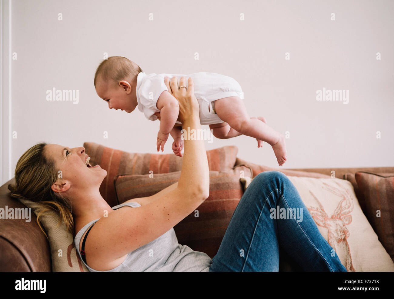 Eine Frau liegt auf dem Sofa mit einem Babymädchen spielen. Stockfoto
