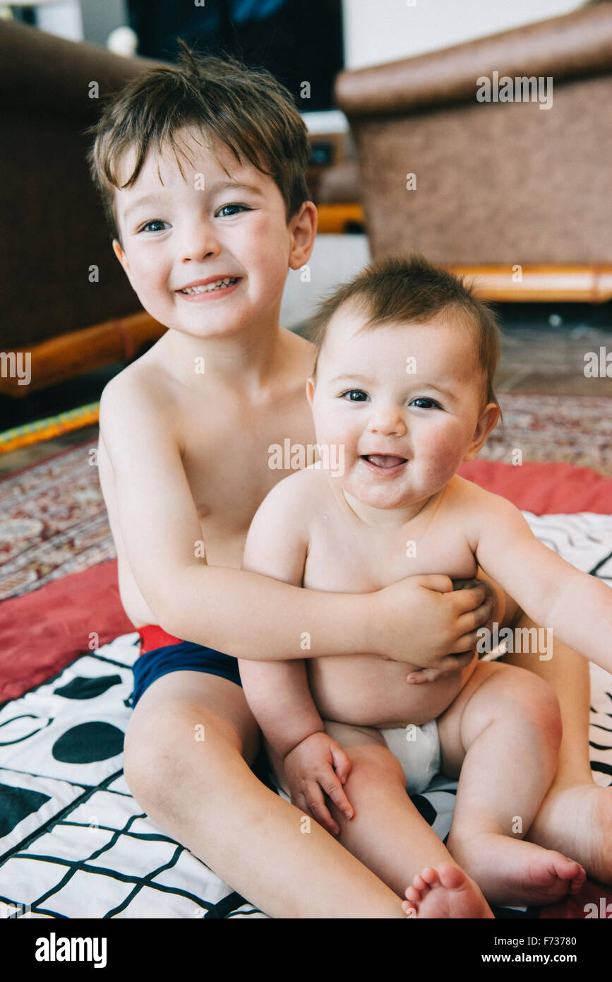 Zwei Geschwister, einen jungen und seine kleine Schwester sitzt auf einem Teppich vor Lachen. Stockfoto
