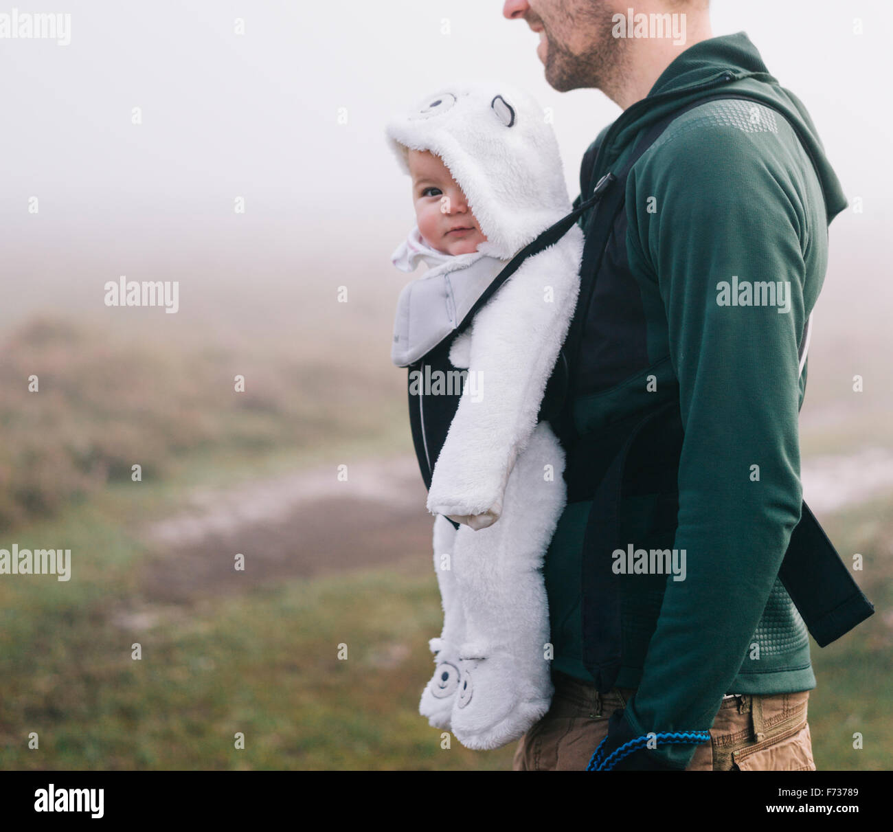 Ein Mann trägt ein Baby im Tragetuch auf seiner Brust, im Freien an einem nebligen Herbsttag Stockfoto