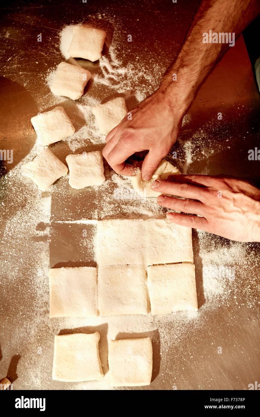 Ein Bäcker arbeiten auf einer bemehlten Arbeitsfläche den vorbereiteten Teig in Quadrate aufzuteilen. Stockfoto
