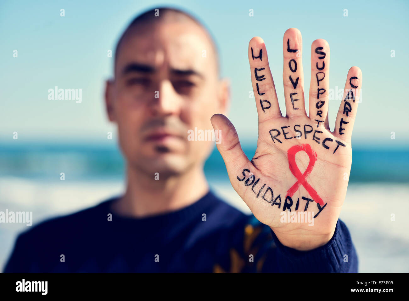 Nahaufnahme der Hand eines jungen kaukasischen Mann mit einem roten Band für den Kampf gegen AIDS, und die Worte malte hilft, lo Stockfoto