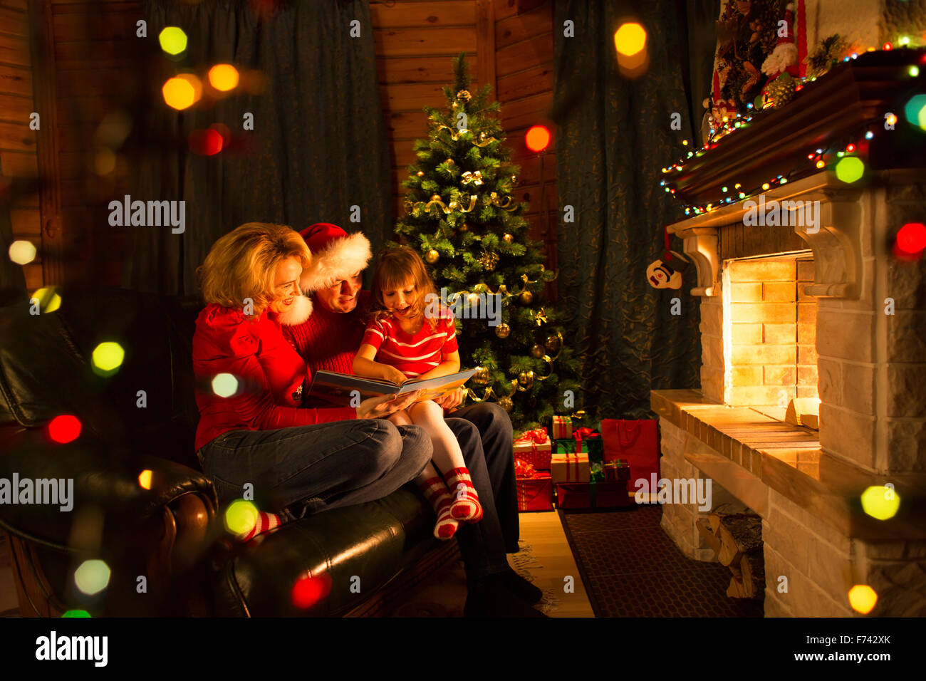 Glückliche Familie, die ein Buch von einem Weihnachtsbaum im gemütlichen Wohnzimmer im winter Stockfoto