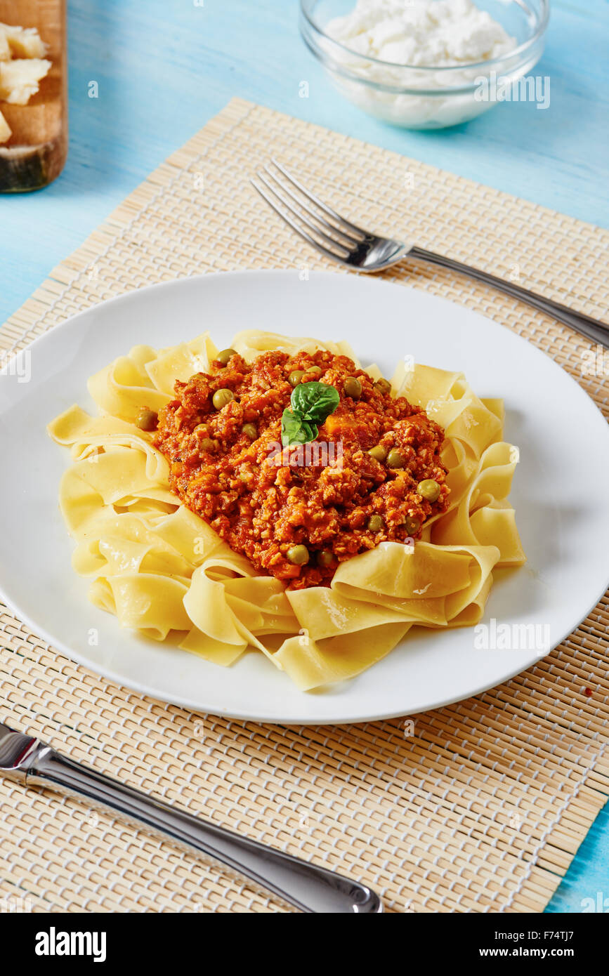 Tagliatelle mit Bolognese-Sauce auf weißen Teller und blauen Holztisch Stockfoto