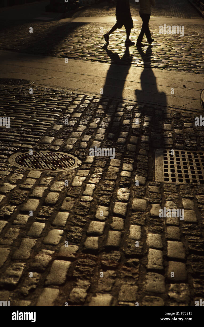 Zwei unkenntlich Jugendliche zu Fuß eine Straße mit Kopfsteinpflaster in Bernstein Nacht Schatten Stockfoto