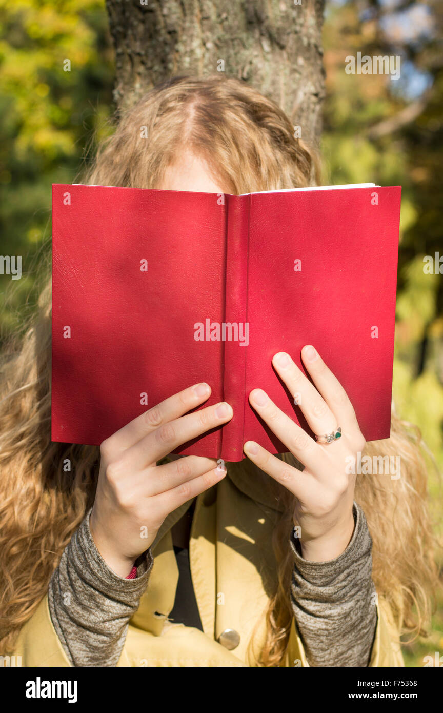 Blondes Mädchen in einem roten Buch in einem Park an einem sonnigen Herbsttag Stockfoto