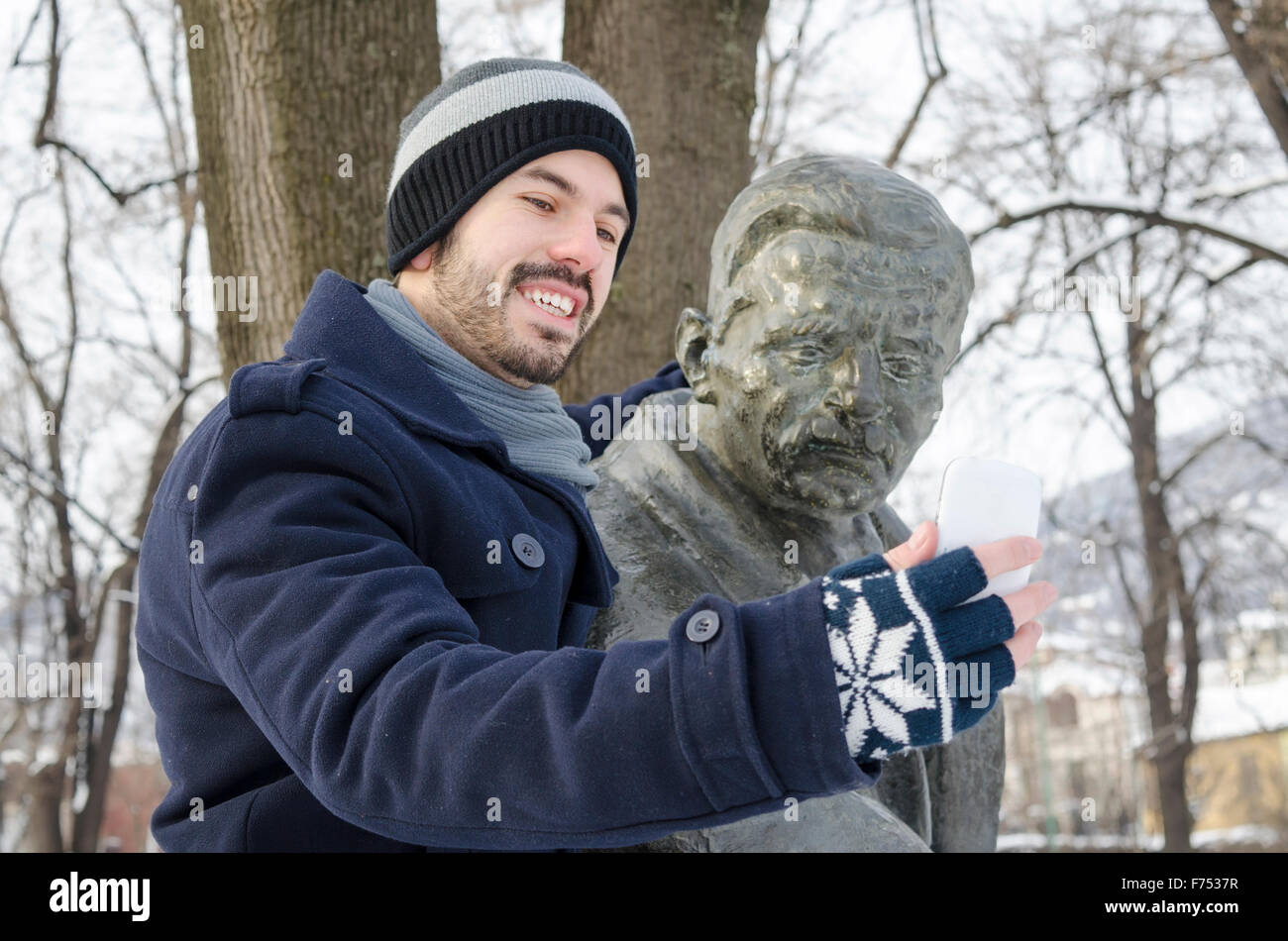 Junge bärtige Mann unter einem Selfie mit einem Denkmal in einem Park an einem sonnigen Wintertag Stockfoto