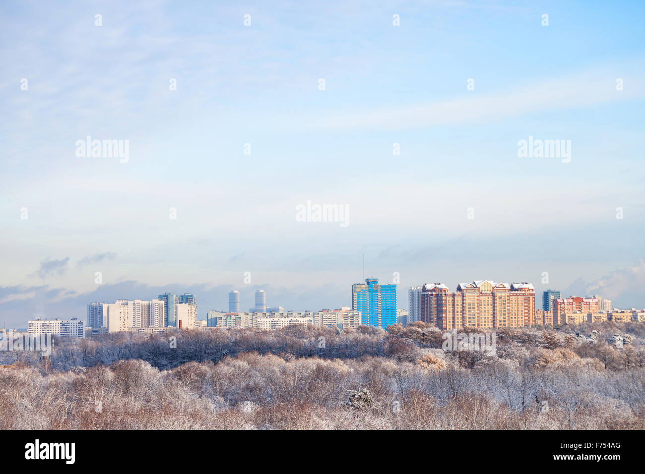 weiße Wolken am blauen Himmel über Schneewald und Stadt im Winter Stockfoto