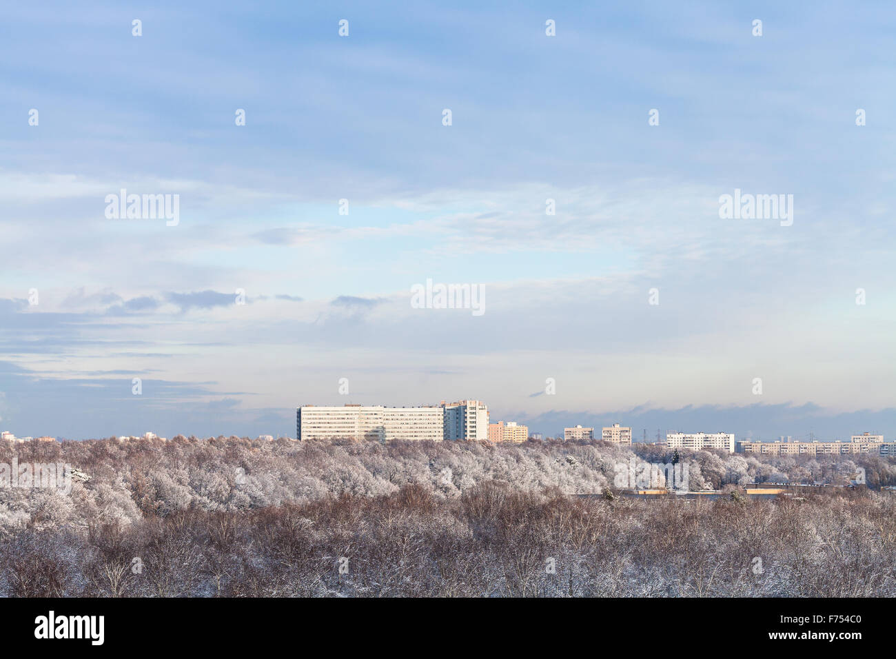 blaue Wolken am blauen Himmel über Schneewald und Stadt im Winter Stockfoto