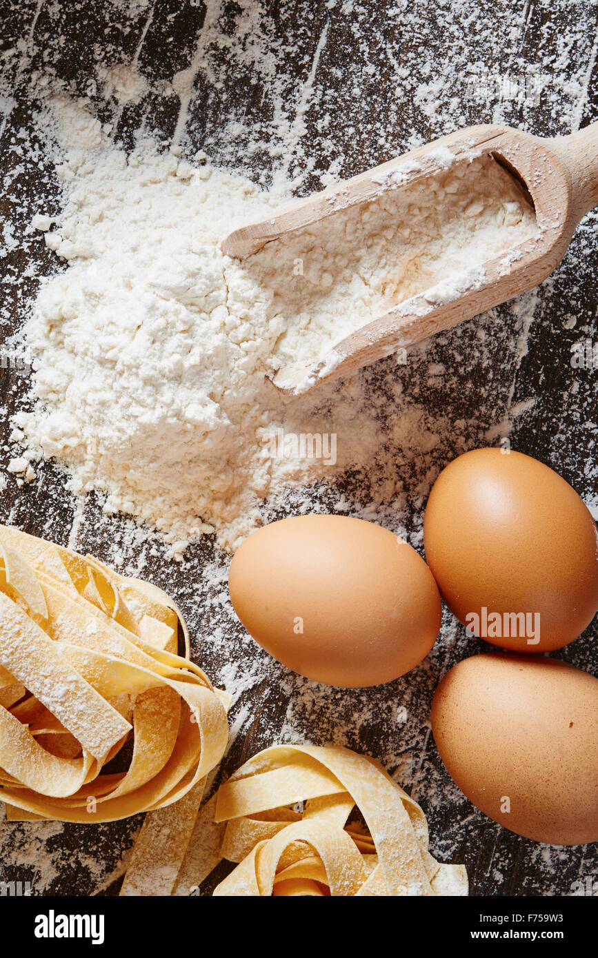 Kochlöffel mit Mehl, Ei und Nudeln auf bemehlten Tisch aus Holz Stockfoto