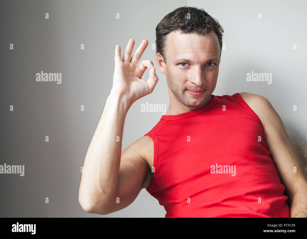 Positiven jungen lächelnder Mann im roten Hemd zeigt Ordnung Geste Stockfoto