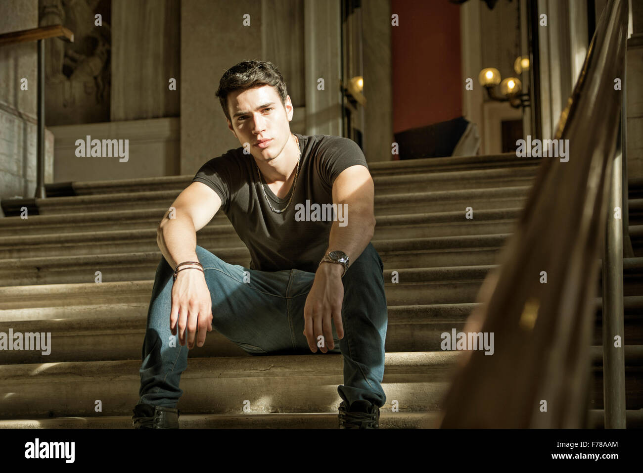 Hübscher Jüngling Stitting auf Treppe im Inneren ein architektonisches elegante alte Gebäude beim Blick in die Kamera Stockfoto