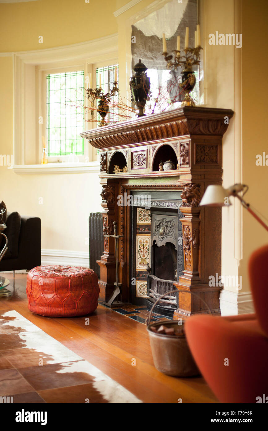 Leder Hocker und Sitz im marokkanischen Stil durch einen geschnitzten hölzernen Kamin im Wohnzimmer mit Holzboden ein einer Tierhaut-Wolldecke Stockfoto