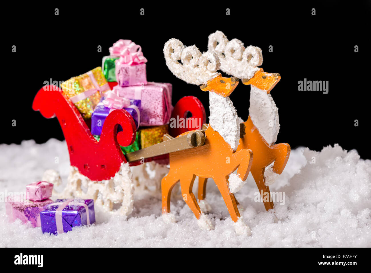 Stillleben mit Weihnachts Dekoration Rentier und Schlitten mit Geschenken im Schnee ist auf schwarzem Hintergrund, Closeup isoliert. Stockfoto